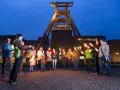 Eine Gruppe von Menschen hält nachts Fackeln vor dem Förderturm der Zeche Zollverein.