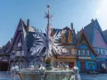 Ein eisiger Brunnen mit Schneeflocken-Dekor vor bunten Häusern, wie in einem **frozen Disneyland**.