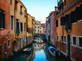 Bunte Häuser säumen einen Kanal in Venedig. Kleine Boote treiben auf dem Wasser. Ein kleiner Bogenbrücke überspannt den Kanal. Das ist, was man in Venedig gesehen haben muss.