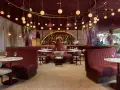 Efteling restaurant mit roten Samt-Sitzbänken, runden Marmortischen und üppigen Blumenarrangements. Hängende Kugelleuchten schaffen eine warme Atmosphäre.