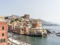 Bunte Häuserfronten am Meer in Genua, Italien. Boote liegen am Ufer, Menschen entspannen sich am Strand.