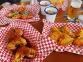 Leckere Cosmo Wings in roten Körbchen, garniert mit Chilis und Schnittlauch. Dazu ein Bier und kleine Beilagen.