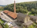 Alte Zechengebäude der Zeche Nachtigall mit einem langen roten Dach, einem hohen Backsteinschornstein und einem historischen Zug.