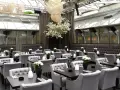 Elegantes Restaurant mit grauen Sitzmöbeln und dunklen Tischen, dekoriert mit weißen Blumen. Ein großer Kirschblütenbaum im Zentrum, beleuchtet von kugelförmigen Lampen. Perfekt für ein Rendezvous, wie ein Oscar-Moment im Apropos.
