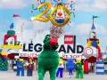 Bunte Konfetti-Explosion bei der Legoland Parade! Ein grüner Drache hält einen roten Lego-Stein hoch, umgeben von Figuren und bunten Türmen.