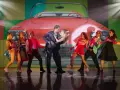 Tänzer in 50er-Jahre-Outfits vor einem roten Oldtimer-Cabriolet. Ein Paar tanzt im Zentrum, umgeben von anderen Darstellern. Ein lebendiger Moment aus Musicals Deutschland.