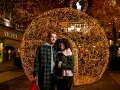 Ein glückliches Paar vor einer riesigen Lichterkugel auf dem weihnachtsmarkt roermond. Geschäfte wie Versace und Ralph Lauren sind im Hintergrund zu sehen.