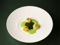 Ammolite speisekarte: Drei grüne Ravioli mit goldbrauner Kruste auf einer leuchtend grünen Sauce, angerichtet auf einem weißen Teller.