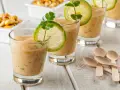Erfrischende Gläser mit cremiger Tigermilch, garniert mit Limettenscheiben und Koriander. Kleine Holzlöffel liegen bereit.