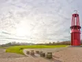 Rote Aussichtsturm auf der Halde Moers, umgeben von grünen Hügeln und einem weiten Himmel mit Wolken.
