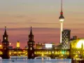 Berlin Kreuzberg bei Sonnenuntergang: Oberbaumbrücke, Fernsehturm und beleuchtete Gebäude spiegeln sich im Wasser.