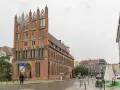 Ein Mann geht durch die regennasse **Stettin Altstadt** an einem Backsteingebäude mit Spitzdächern vorbei.