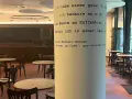Gemütliches **cafe vegan** mit vielen Tischen und Stühlen. Eine Säule ziert ein Zitat von Hermann Kesten über das Kaffeehaus.