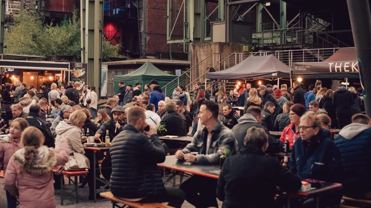 Menschen genießen Speisen und Getränke auf dem Street Food Festival Duisburg. Viele Besucher sitzen an langen Tischen und unter Zelten.