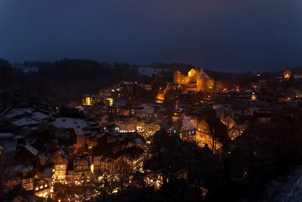 Monschau im Winter: Fachwerkhäuser und Burg leuchten im Dunkeln, wie auf einem magischen Weihnachtsmarkt.