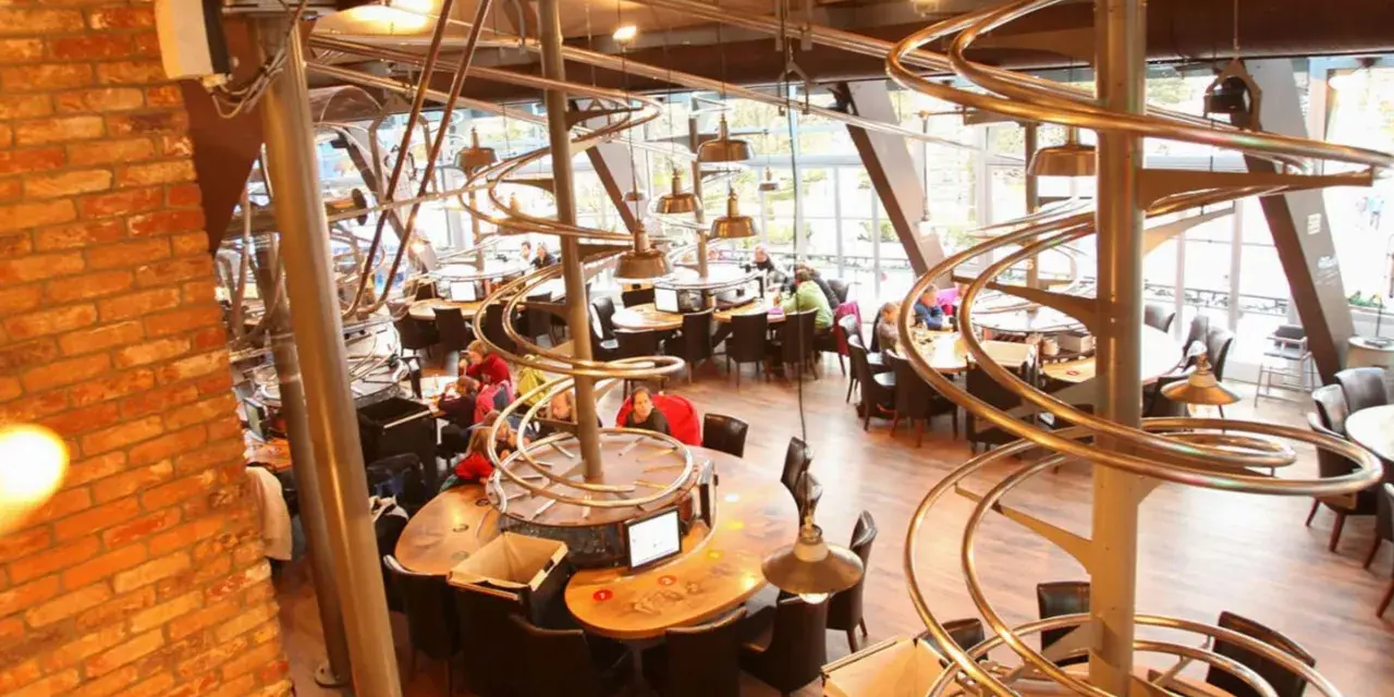 Einzigartiges Restaurant im Europa-Park mit Achterbahn-Schienen als Deko. Gäste sitzen an runden Tischen unter den metallischen Kurven.