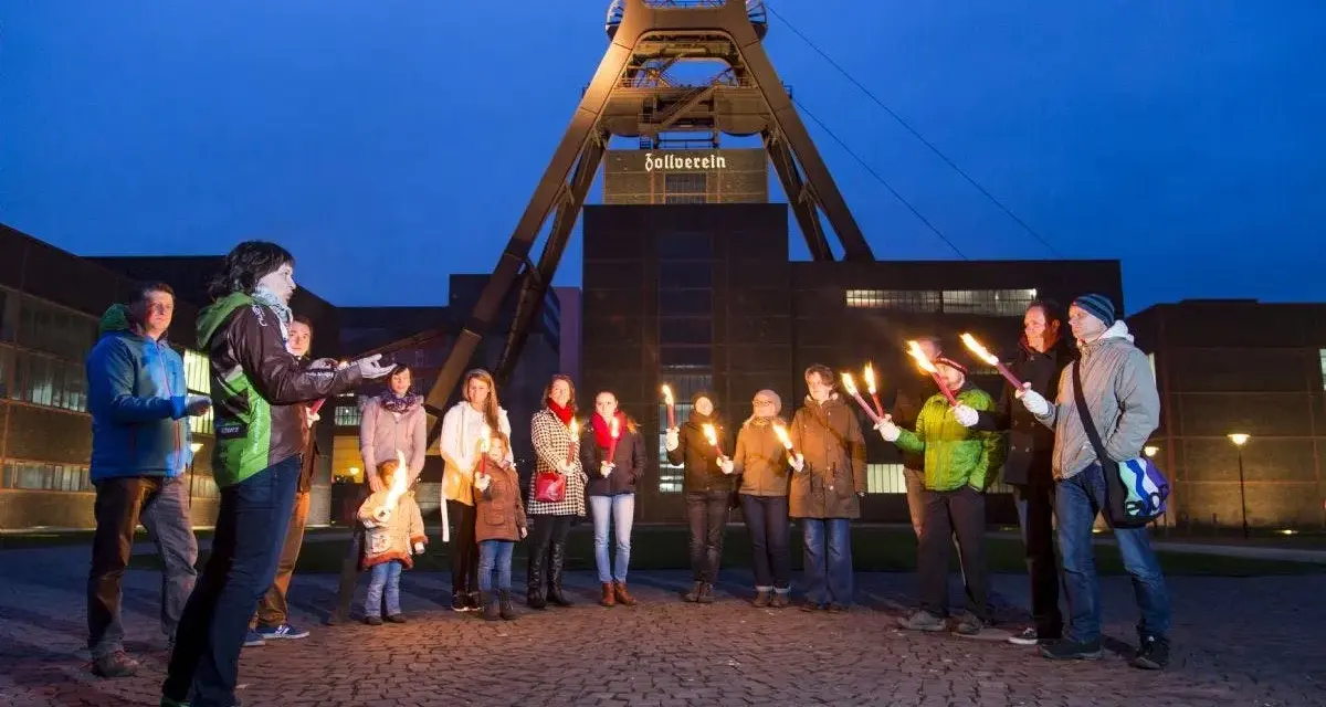 Eine Gruppe von Menschen hält nachts Fackeln vor dem Förderturm der Zeche Zollverein.