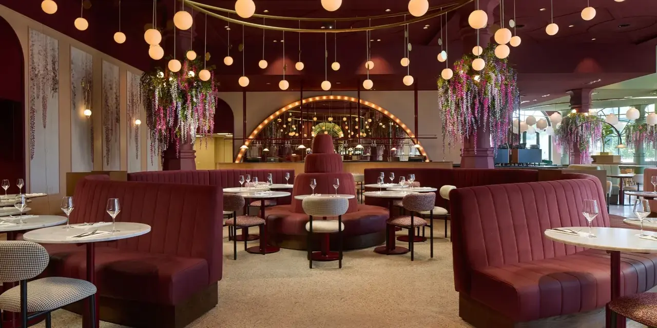 Efteling restaurant mit roten Samt-Sitzbänken, runden Marmortischen und üppigen Blumenarrangements. Hängende Kugelleuchten schaffen eine warme Atmosphäre.