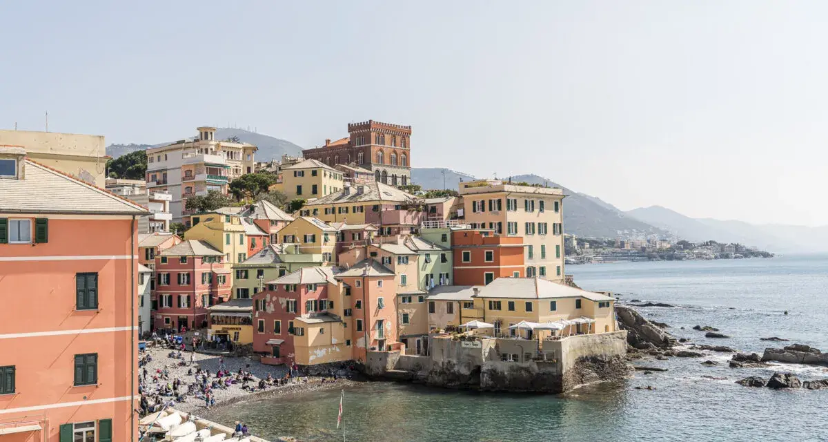 Bunte Häuserfronten am Meer in Genua, Italien. Boote liegen am Ufer, Menschen entspannen sich am Strand.