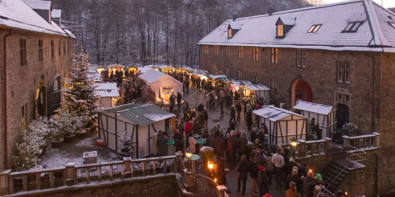 Schneebedeckter Weihnachtsmarkt in einer Burg, ein echter Geheimtipp NRW. Besucher schlendern zwischen festlich beleuchteten Buden.
