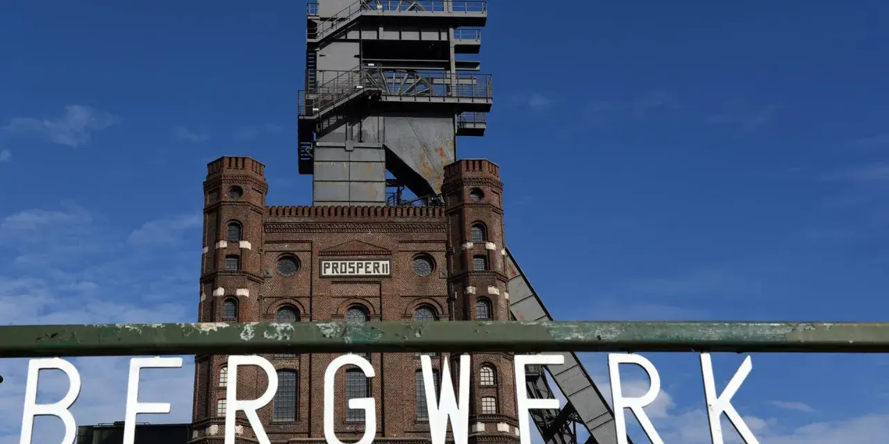 Das alte Bergwerk Prosper Haniel mit seinem markanten Förderturm ragt gegen einen blauen Himmel auf.