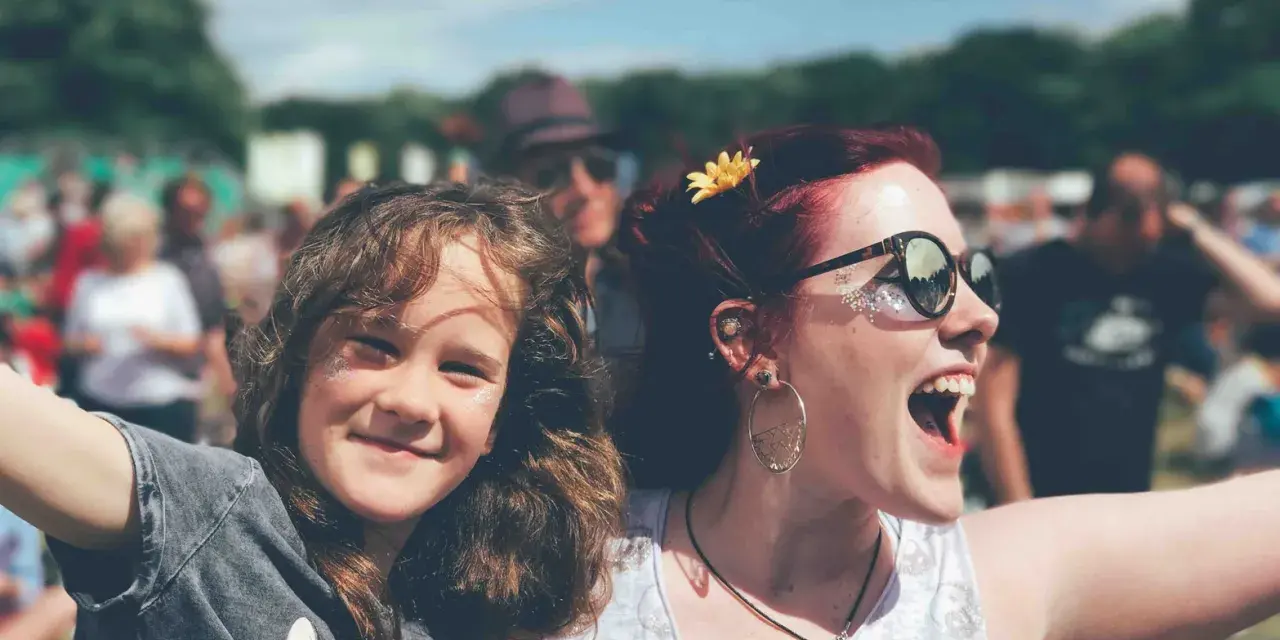 Zwei lachende Frauen, eine davon ein Kind, genießen das vivawest family festival. Glitzer auf den Wangen und eine Blume im Haar.
