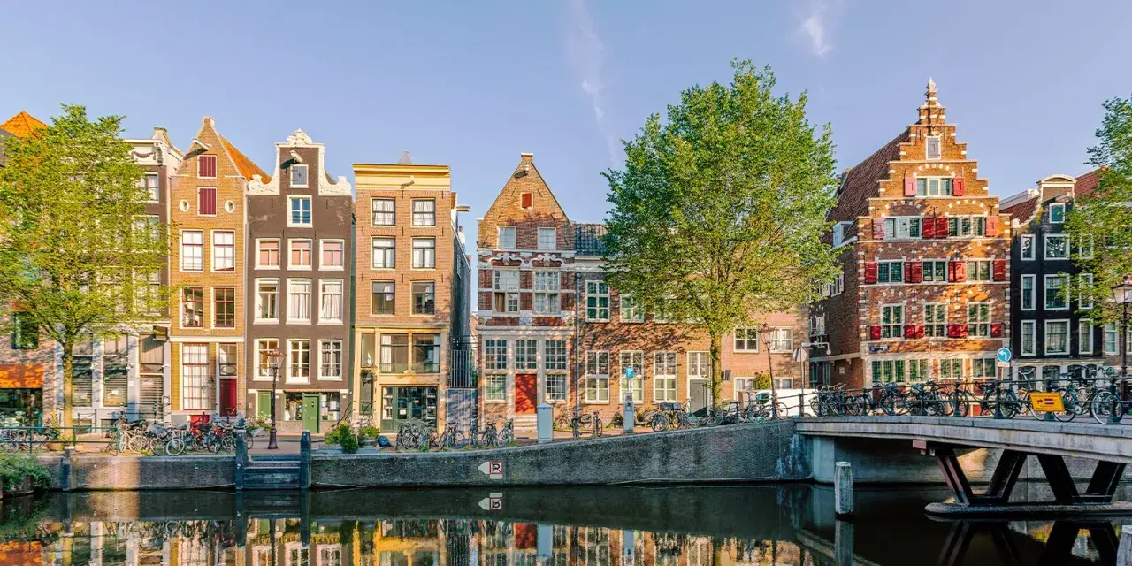 Bunte Grachtenhäuser spiegeln sich im Wasser. Fahrräder säumen den Kanal. So viel **was kann man in Amsterdam machen**!