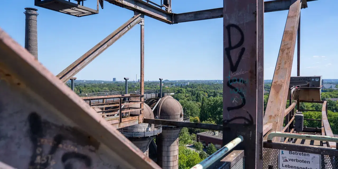 Industrielles Erbe in Duisburg: Rostige Stahlkonstruktionen und Kuppeln des Landschaftsparks Nord, mit Blick auf grüne Bäume und Gebäude.