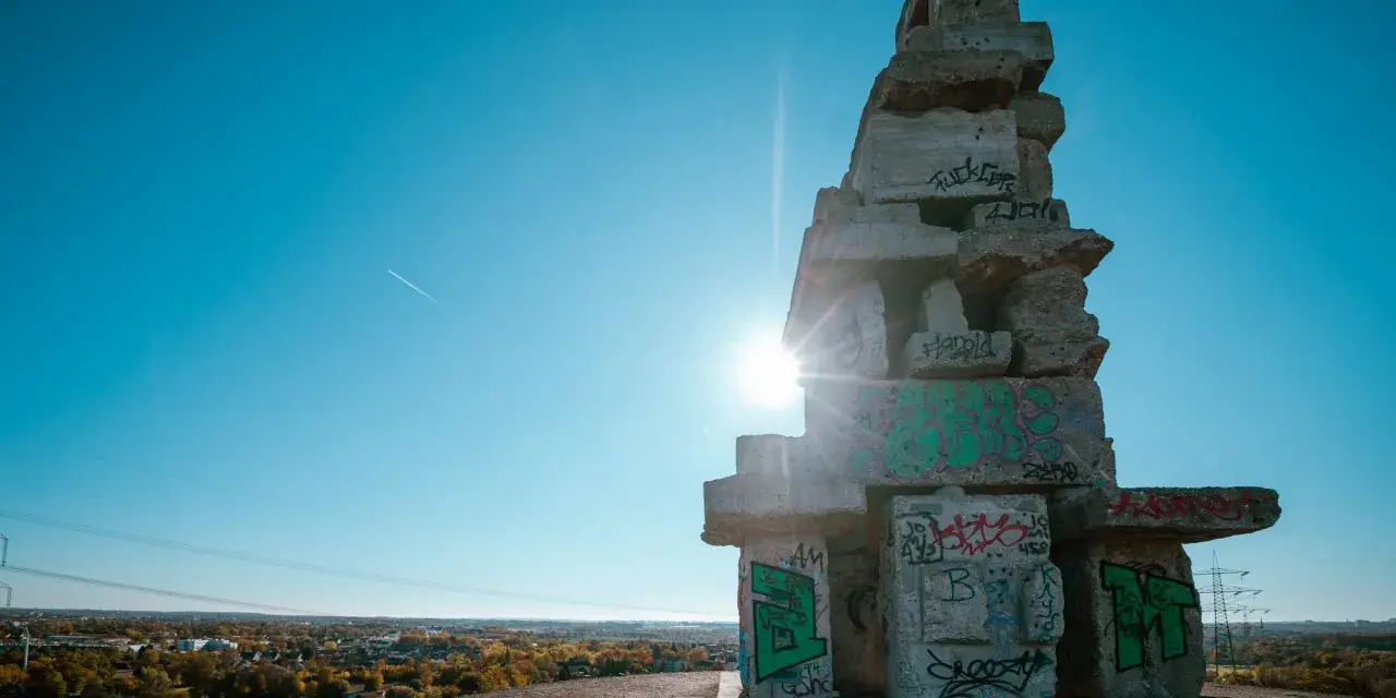 Sonnenstrahlen brechen durch eine Betonkonstruktion auf der Halde Rheinelbe, die mit Graffiti übersät ist.