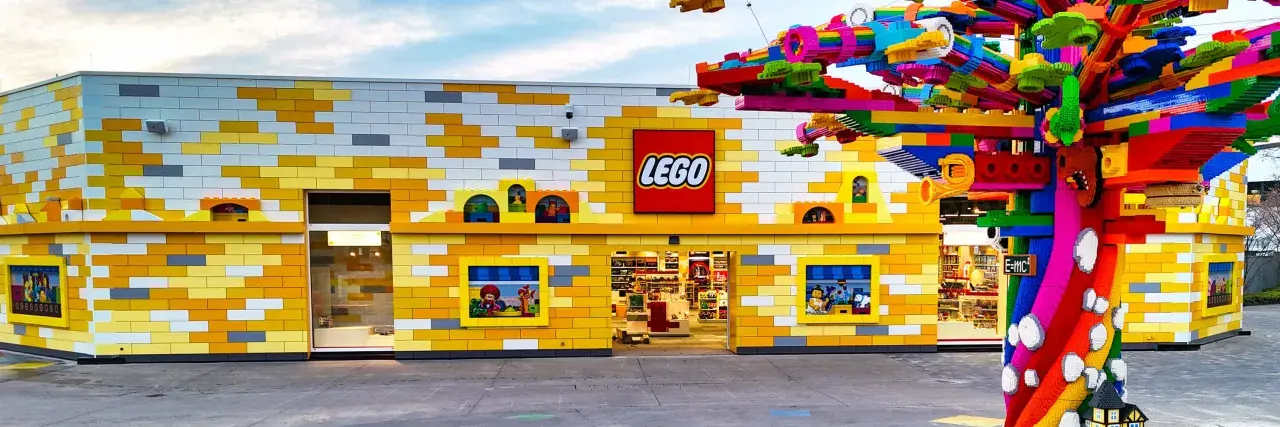Bunte Lego-Steine schmücken das Gebäude und einen Baum. Ein lebendiger Lego-Freizeitpark lädt zum Spielen ein.