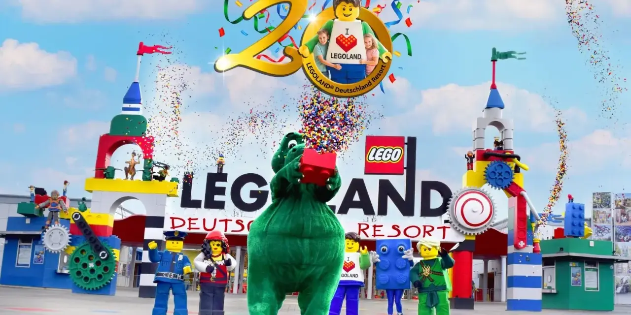 Bunte Konfetti-Explosion bei der Legoland Parade! Ein grüner Drache hält einen roten Lego-Stein hoch, umgeben von Figuren und bunten Türmen.