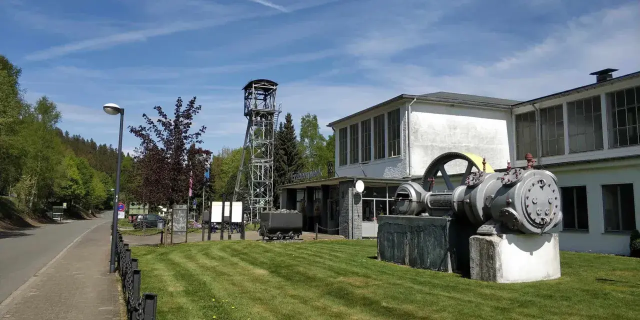 Ein historisches Bergwerk lädt zum Bergwerk besichtigen ein. Eine Förderturmanlage und alte Maschinen stehen vor dem Gebäude.