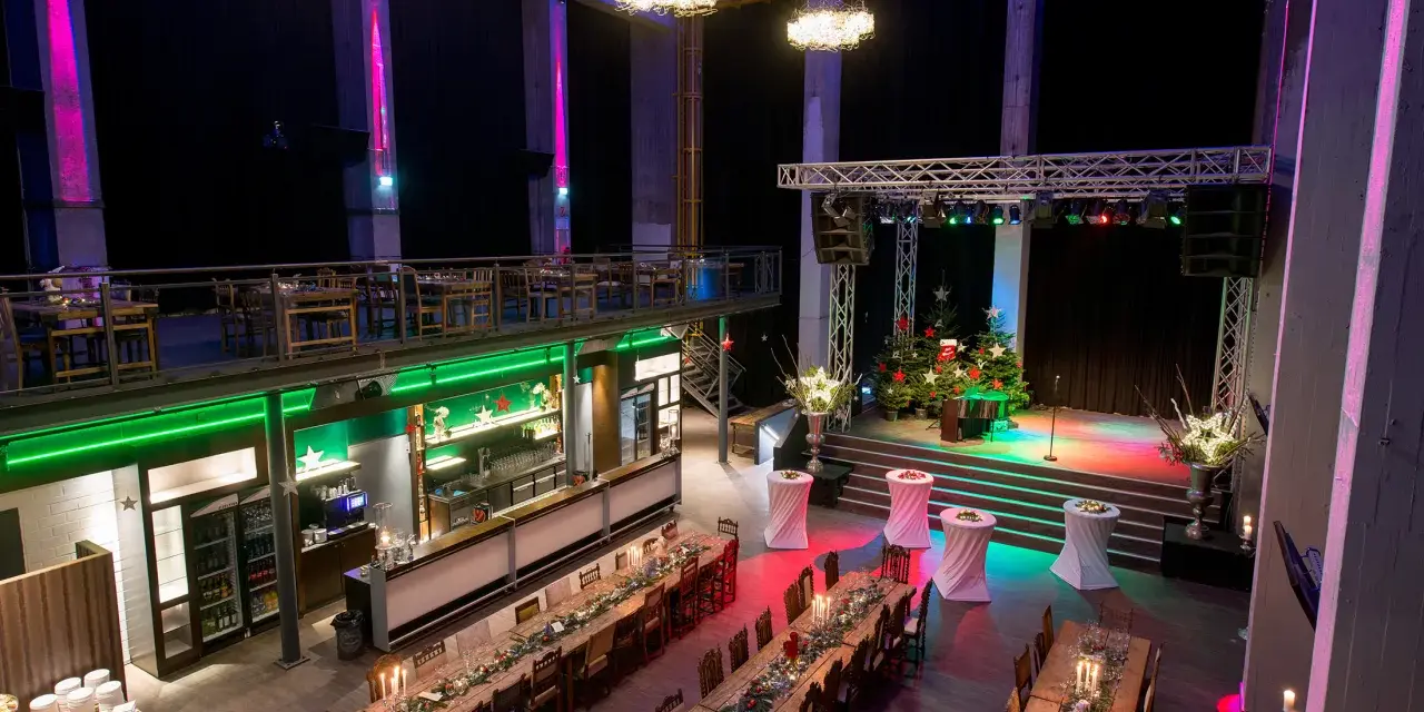 Festliche Weihnachtsstimmung in der Motorworld Zeche Ewald: festlich geschmückte Tische, Bühne mit Weihnachtsbäumen und stimmungsvolle Beleuchtung.