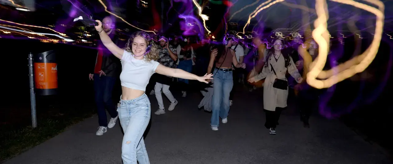 Junge Leute mit Kopfhörern, die im Dunkeln tanzen gehen, umgeben von bunten Lichtspuren.