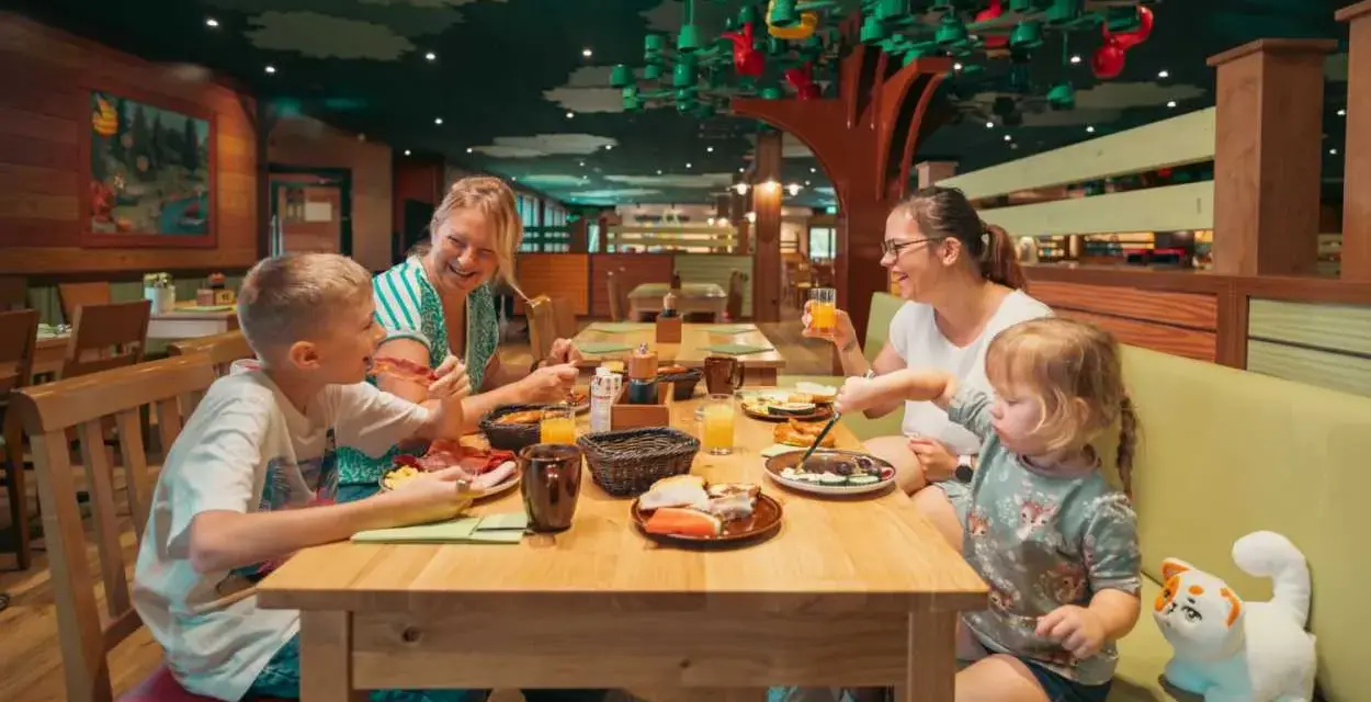 Familie genießt ein fröhliches Frühstück in einem fantasievollen Legoland Restaurant mit Baumdeko.