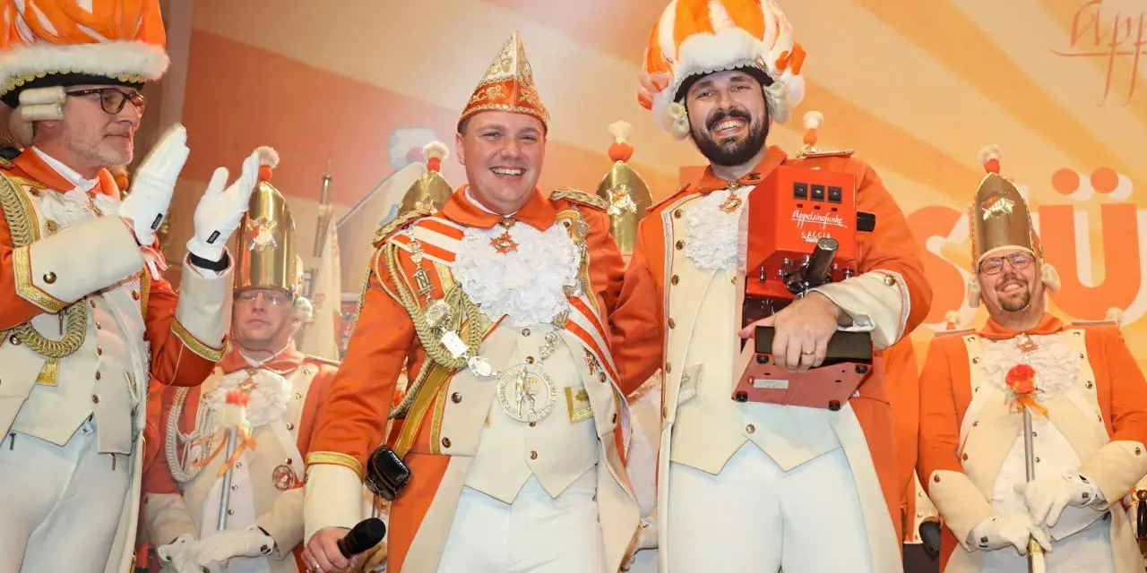 Narren in bunten Kostümen feiern jecke Tage. Ein Mann hält eine Kaffeemaschine, die anderen tragen prunkvolle Uniformen und Federhüte.