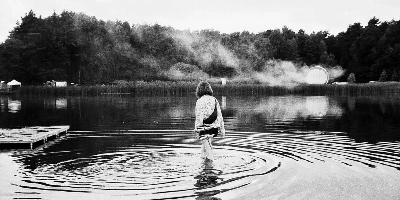 Ein Mädchen watet im Wasser, während im Hintergrund Nebel und eine Lichtinstallation zu sehen sind. Ein friedlicher Moment beim nachtigall festival.