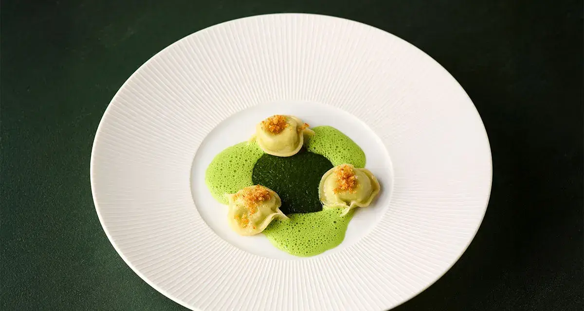 Ammolite speisekarte: Drei grüne Ravioli mit goldbrauner Kruste auf einer leuchtend grünen Sauce, angerichtet auf einem weißen Teller.
