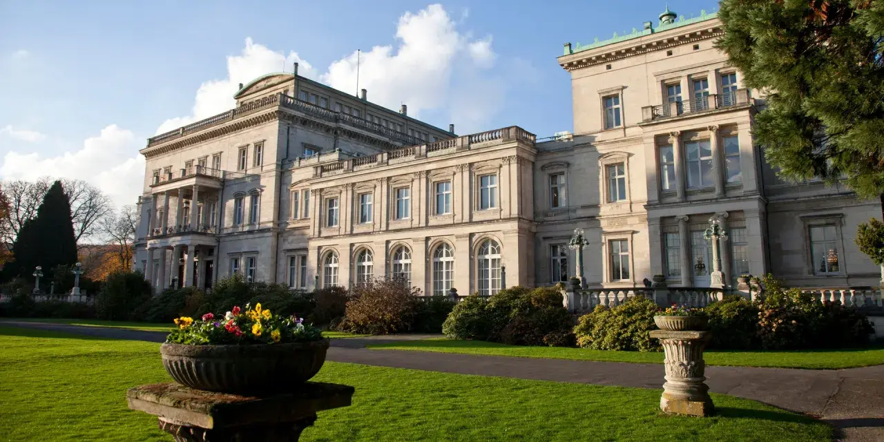 Prachtvolle Krupp Villa mit gepflegtem Garten und Blumenkübeln im Sonnenschein.
