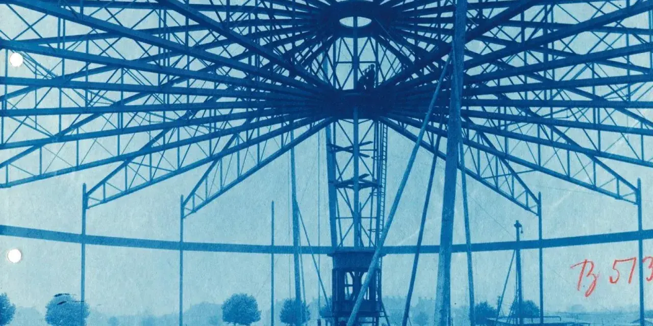 Bau des Riesenrades am GHH Oberhausen. Die Stahlkonstruktion ragt in den Himmel, Arbeiter sind auf der Spitze zu sehen.