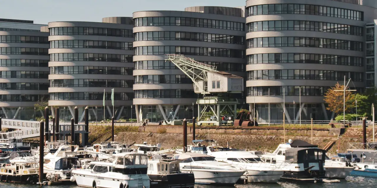 Moderne Gebäude am Duisburg Innenhafen mit vielen Yachten im Wasser. Ein alter Kran erinnert an die industrielle Vergangenheit.
