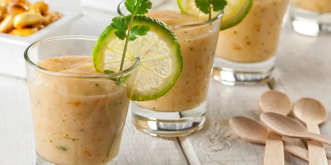 Erfrischende Gläser mit cremiger Tigermilch, garniert mit Limettenscheiben und Koriander. Kleine Holzlöffel liegen bereit.