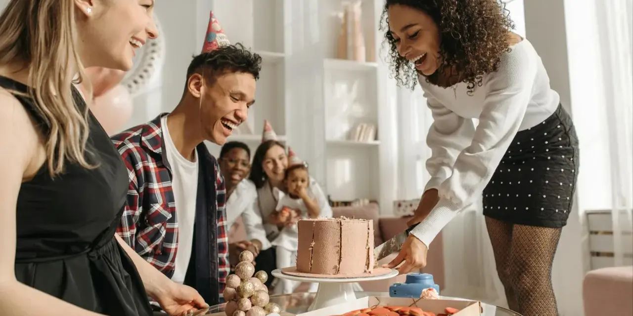 Fröhliche Gruppe feiert den 30. Geburtstag mit Kuchen und Keksen. Alle tragen Partyhüte und lachen ausgelassen.