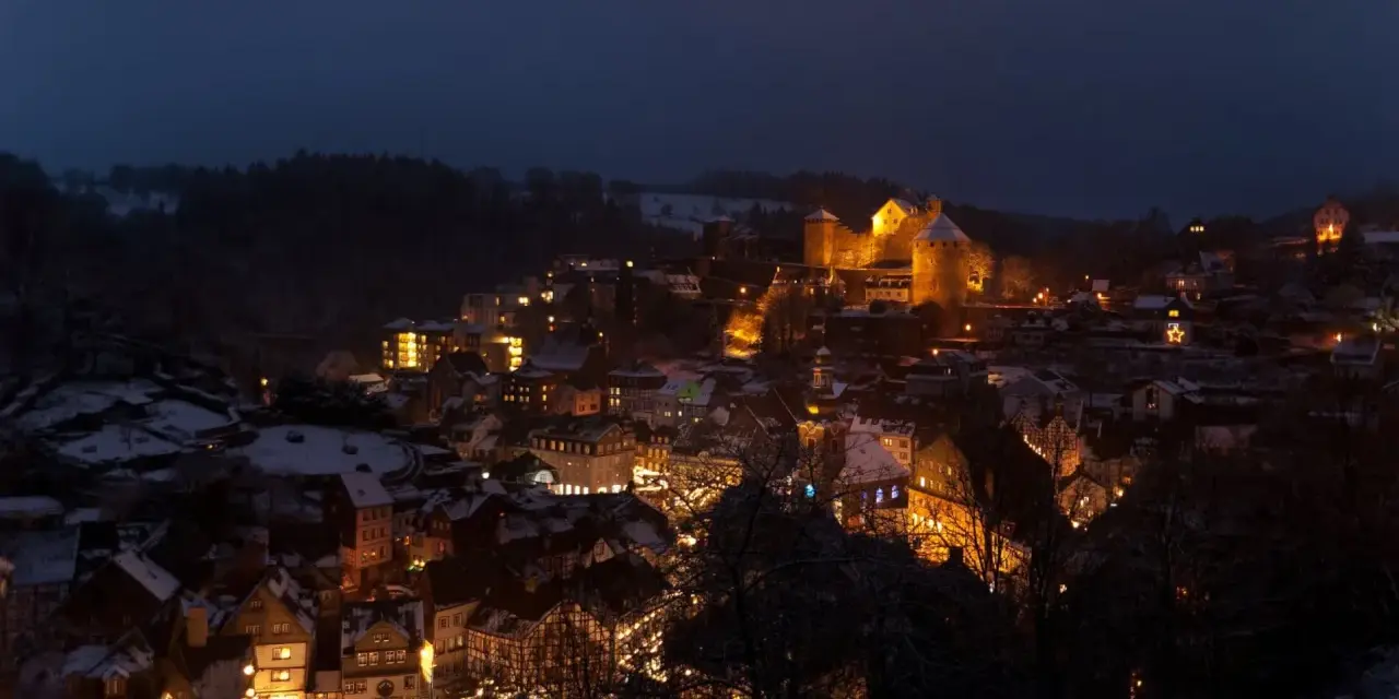 Monschau im Winter: Fachwerkhäuser und Burg leuchten im Dunkeln, wie auf einem magischen Weihnachtsmarkt.