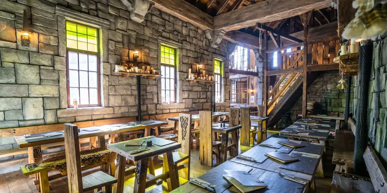 Rustikale Phantasialand Taverne mit Steinwänden, Holztischen und Bänken, Kerzenlicht und mittelalterlichem Flair.