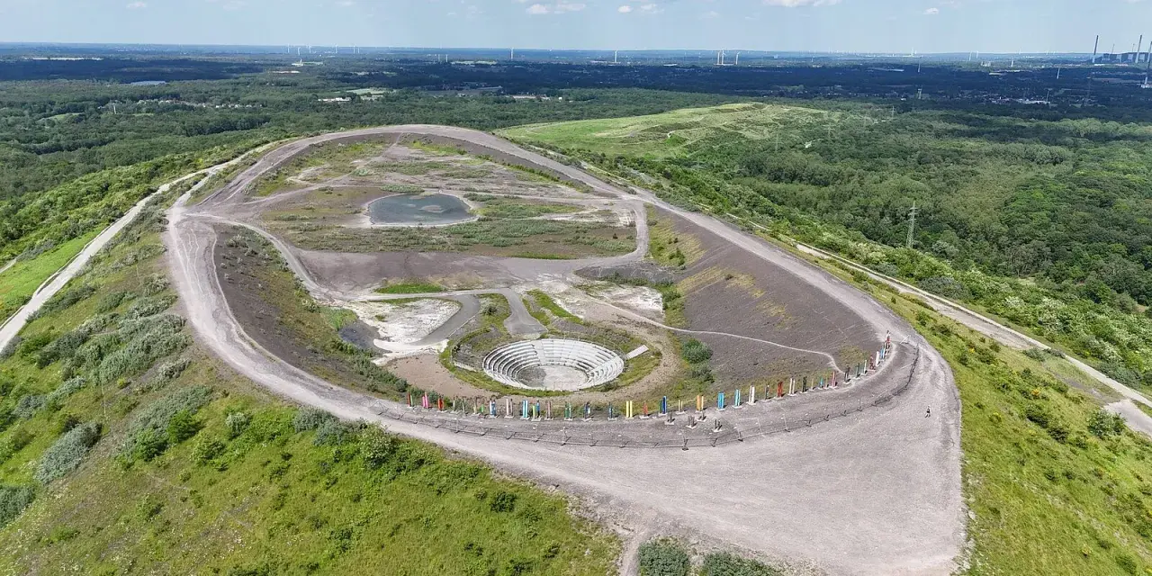 Die Halde Haniel mit ihrem Amphitheater und bunten Stelen, umgeben von grüner Natur und Windrädern in der Ferne.