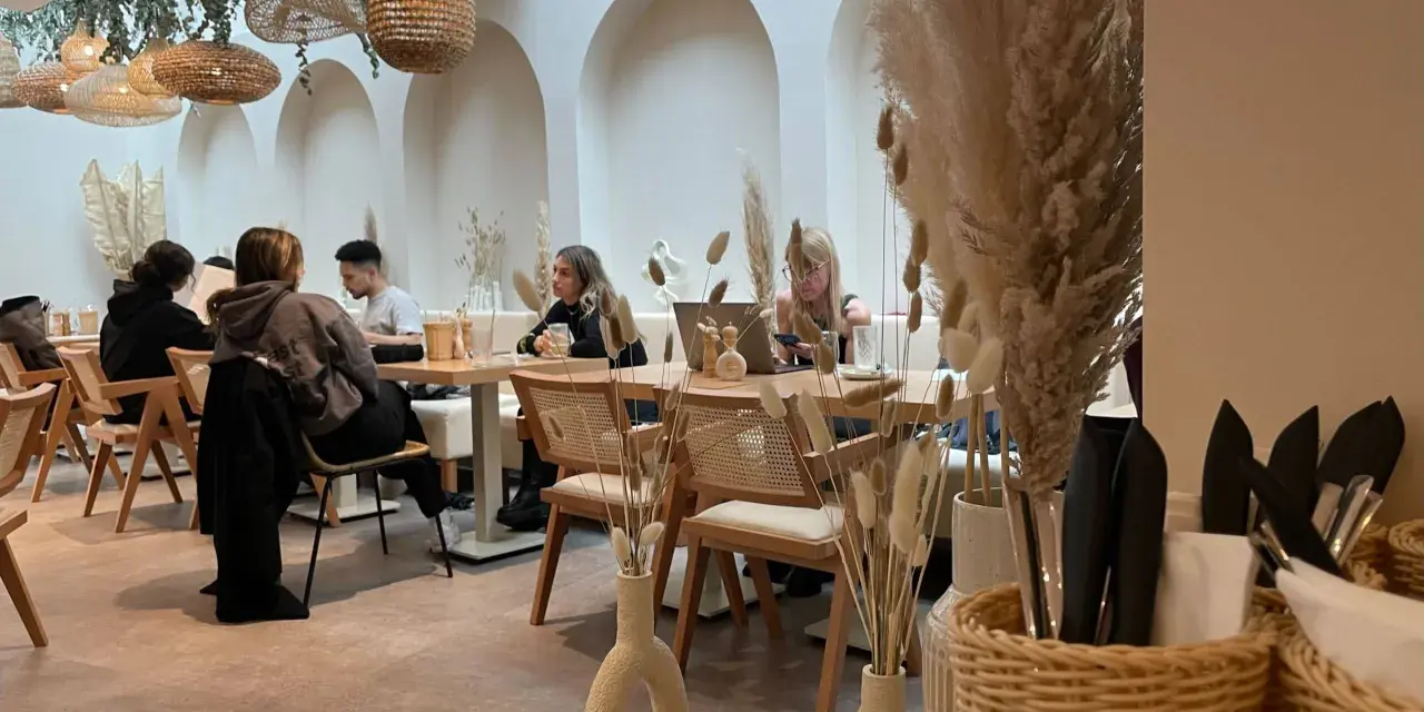 Gemütliches Café mit Boho-Deko, geflochtenen Lampen und Trockenblumen. Gäste genießen ihren soul brunch in entspannter Atmosphäre.