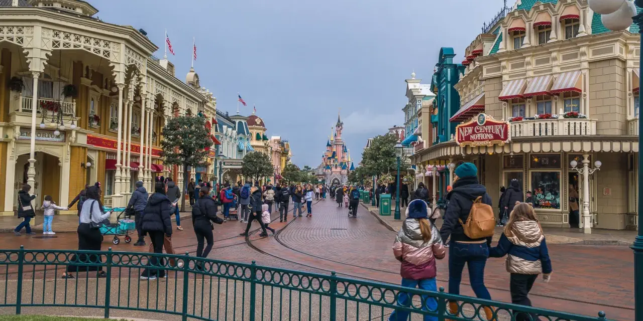 Menschen schlendern die Hauptstraße entlang, vorbei an Geschäften und dem Schloss. Ein Tag im Disneyland, vielleicht mit einem Disneyland Fastpass für die Attraktionen.