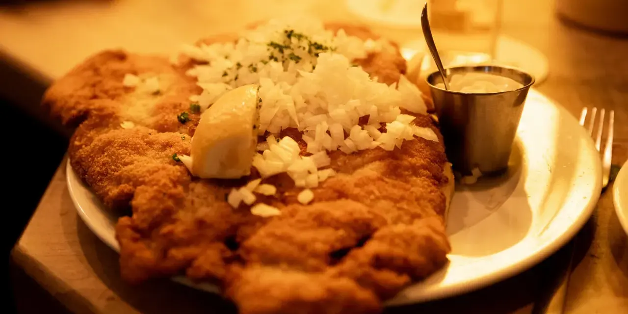 Ein knuspriges Schnitzel mit Zwiebeln und Zitrone, wie bei Oma Kleinmanns. Dazu ein Dip und ein Glas Wasser.