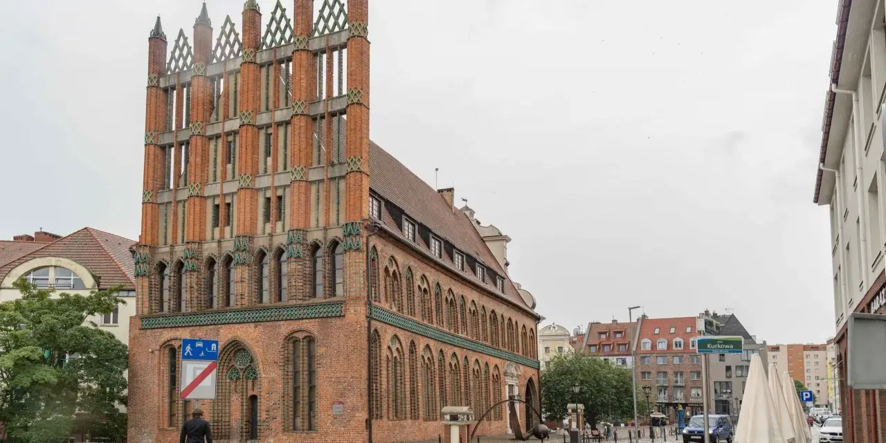 Ein Mann geht durch die regennasse **Stettin Altstadt** an einem Backsteingebäude mit Spitzdächern vorbei.